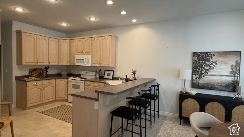 Kitchen featuring light wood-finish cabinetry, white appliances, recessed lighting, and a breakfast bar