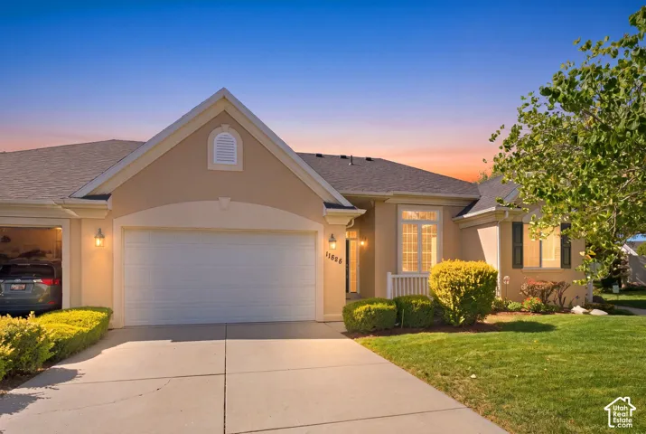 Stucco exterior with an attached two-car garage, pitched shingle roof, and a concrete driveway