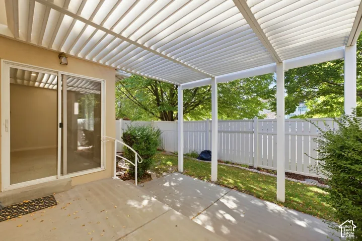 Concrete patio featuring a slatted pergola, sliding glass door, and white picket fencing