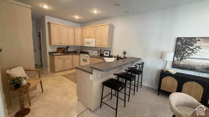 Kitchen featuring light wood-finish cabinetry, white appliances, and a counter-height breakfast bar
