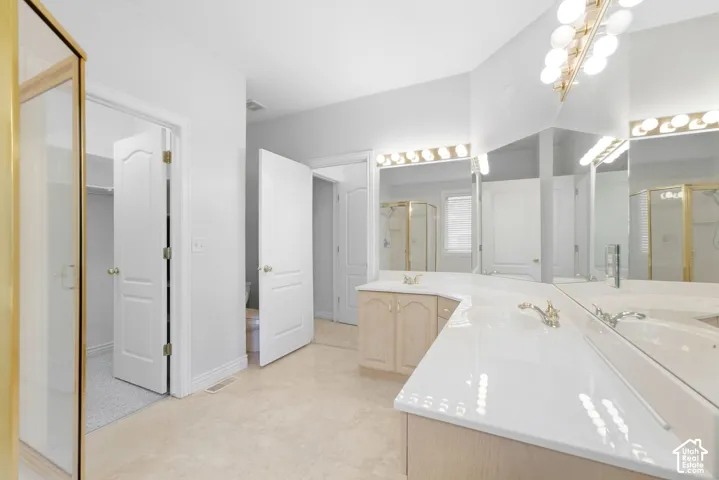 Primary Bathroom, Dual vanity with integrated sinks, expansive mirror, decorative wall sconces, wood-finish cabinetry, and glass-enclosed shower