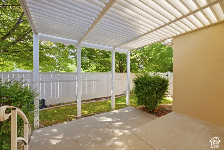 Covered patio with concrete surface, white slatted pergola, white privacy fence, and manicured landscaping