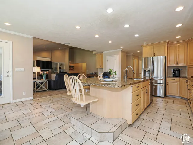 Kitchen featuring light wood cabinetry, recessed lighting, stainless steel refrigerator, and a granite-finish island with integrated seating