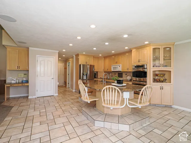 Expansive kitchen featuring light wood cabinetry, stainless steel appliances, recessed lighting, and a large central island with a multi-level countertop