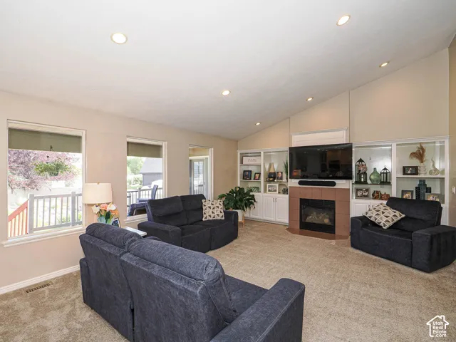 Vaulted ceilings with recessed lighting, integrated fireplace with tile surround, built-in shelving, white trim, and multiple windows