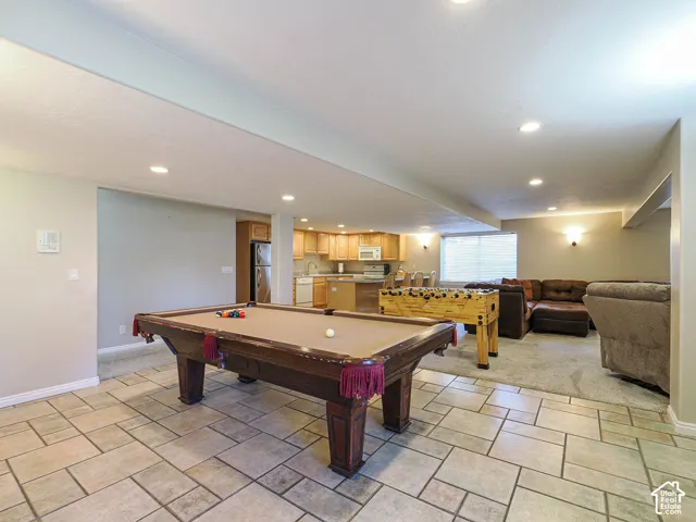 Spacious entertainment area featuring a tiled floor, recessed lighting, and a partial kitchen with wood cabinetry