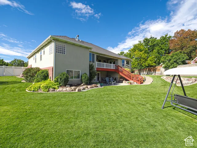 Expansive backyard featuring a manicured lawn, tiered landscaping with natural rock accents, a patio area, and an upper-level deck with red railings
