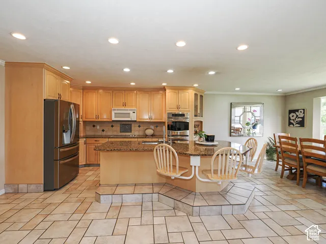 Kitchen featuring recessed lighting, extensive wood cabinetry, stainless steel appliances, a tiled backsplash, and a multi-level island with seating