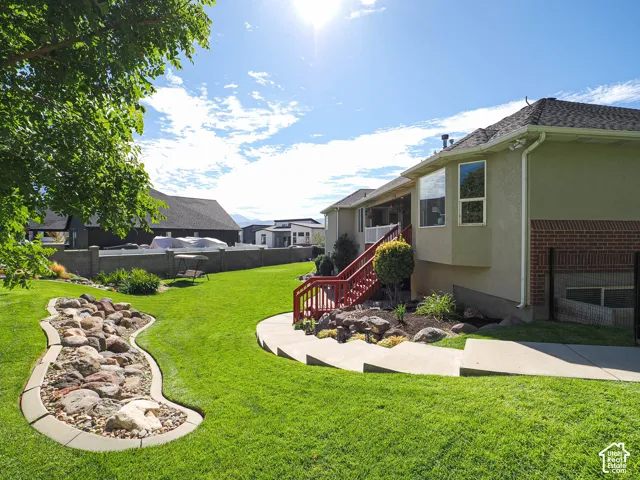 Expansive green lawn with a decorative rock feature, concrete walkway, and red-painted exterior stairs