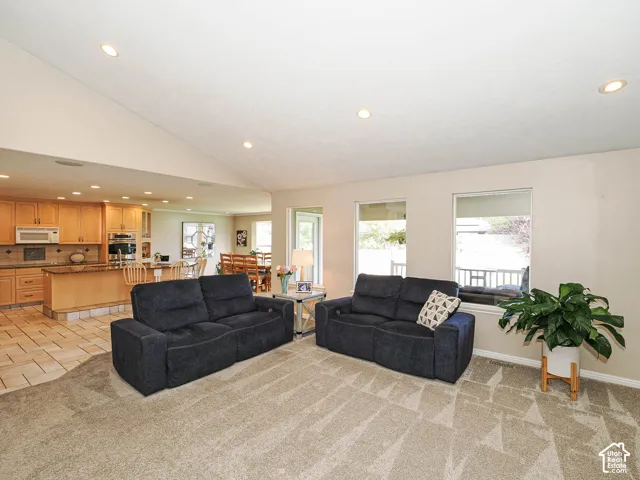 Open-concept living space featuring vaulted ceilings with recessed lighting, a kitchen with wood cabinetry and tile flooring, and multiple windows