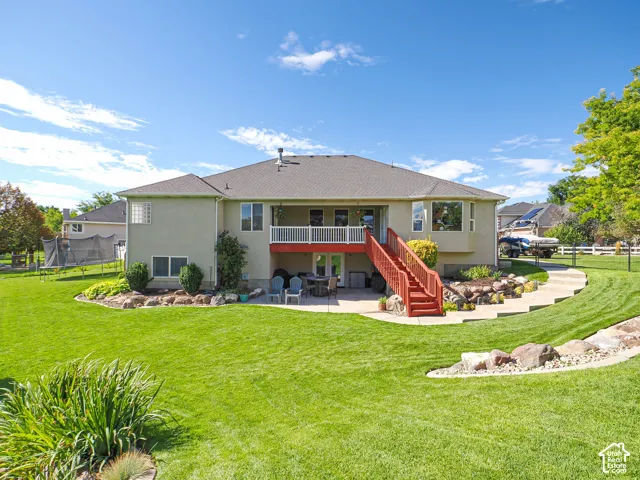 Expansive green lawn with established landscaping beds, a multi-level deck with white railings, and a lower-level patio