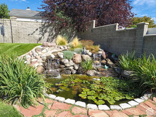 Manicured lawn with a tiered rock waterfall feature, a pond with lily pads, and mature landscaping