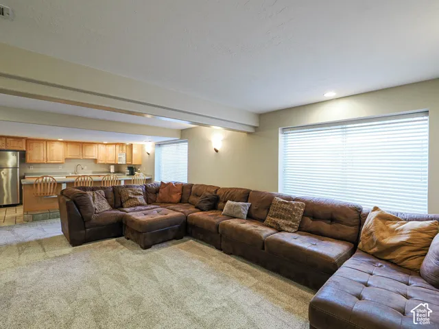 Carpeted living area with recessed lighting, integrated kitchen bar, stainless steel refrigerator, and wood-finish cabinetry
