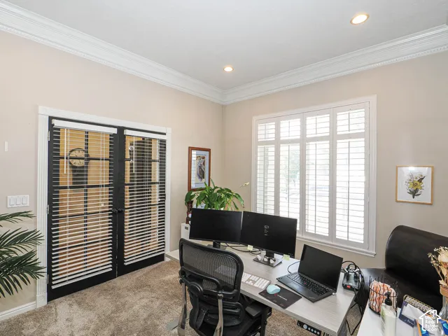 Recessed lighting illuminates a room featuring substantial crown molding, plantation shutters, and a pair of black French doors with integrated blinds