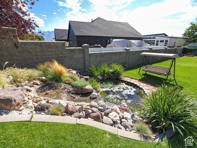 Landscaped backyard featuring a stone water feature, a pond with aquatic plants, and a manicured lawn