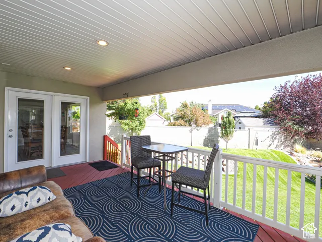 Covered porch featuring white double-pane French doors, a red wood-finish deck, white railing, and recessed lighting