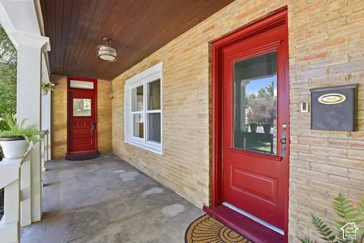 Brick exterior with a covered porch featuring a wood-panel ceiling, white railings, and a red entry door with glass paneling