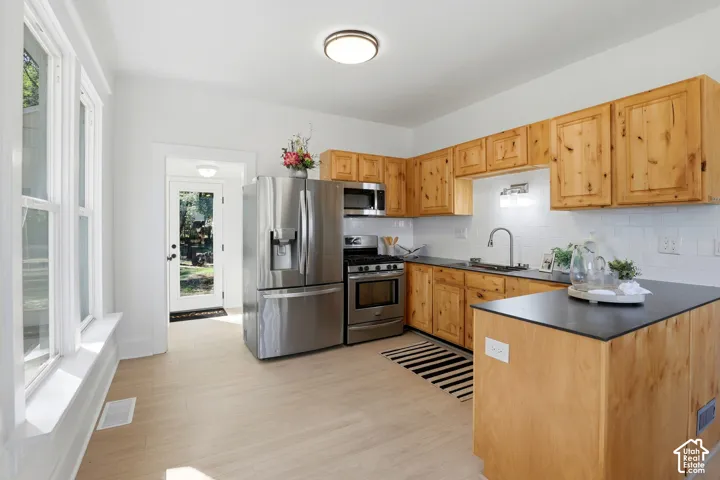 Natural wood cabinetry with dark countertops, stainless steel appliances, and a white subway tile backsplash