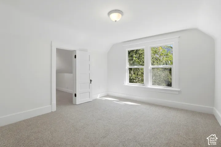 Light-filled room featuring a double window, vaulted ceiling, neutral carpeting, and a flush-mount light fixture