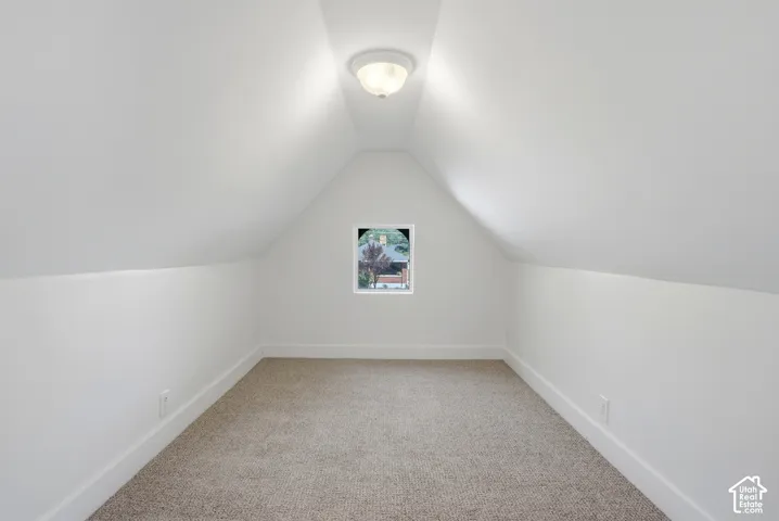 Attic space with sloped ceilings, a single window, and carpet flooring