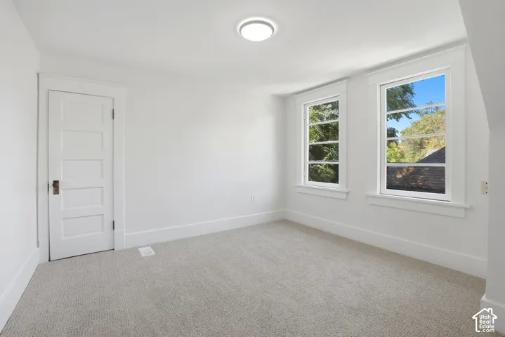 Neutral wall paint, plush carpet flooring, two double-hung windows, and a flush mount ceiling light