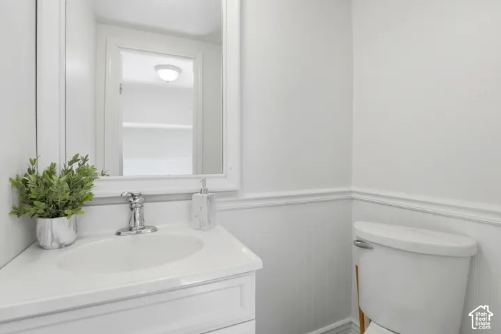 White vanity with integrated sink, chrome faucet, wall-mounted mirror, and beadboard wainscoting