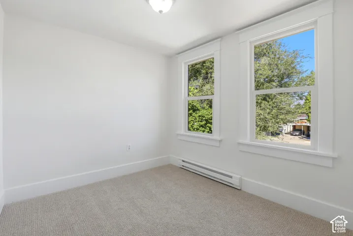 Carpeted room featuring dual windows with white trim, a baseboard heater, and a flush mount ceiling light