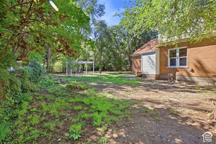 Expansive yard featuring mature trees, a white pergola, and brick exterior