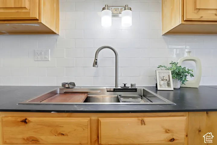 Stainless steel workstation sink with a cutting board insert, brushed nickel gooseneck faucet, black countertop, white subway tile backsplash, and natural wood cabinetry