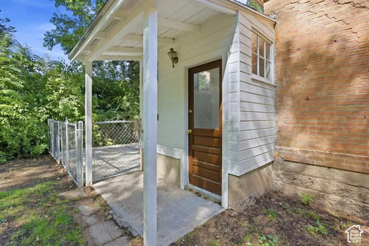 Covered entry featuring a wood-panel door with glass inset, exterior wall sconce, and white siding