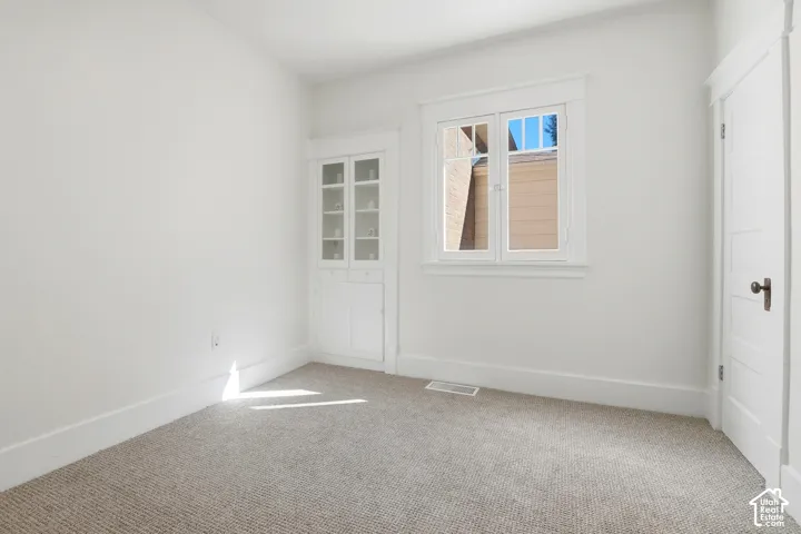 Recessed built-in cabinetry with glass doors, white trim, window with white casing, and light-colored carpeting