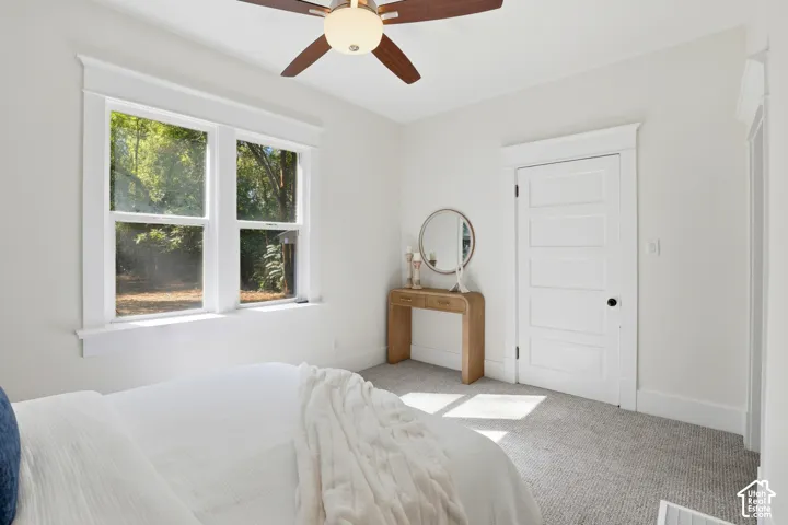 Ceiling fan with light fixture, double-hung windows, paneled interior door, and light-colored carpeting