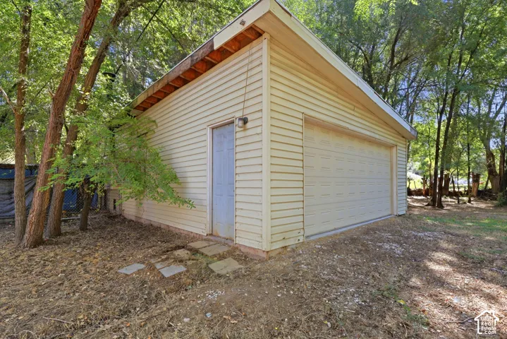 Detached garage with horizontal siding, a single overhead door, an exterior side door, and exterior wall lighting
