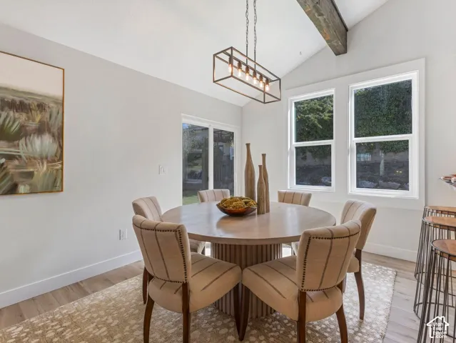 Vaulted ceiling with an exposed wood beam, large windows, wood-finish flooring, and a sliding glass door