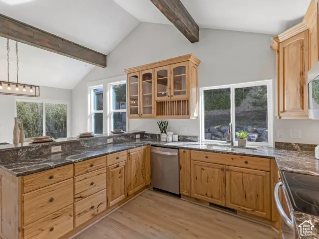 Vaulted ceiling with exposed wood beams, wood-finish flooring, granite countertops, natural wood cabinetry, and stainless steel appliances