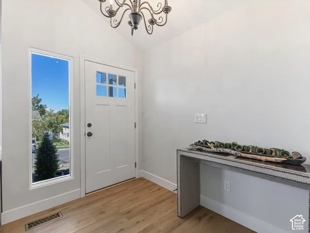Entryway featuring wood-finish flooring, a white paneled door with divided lites, a fixed side lite, and a decorative chandelier
