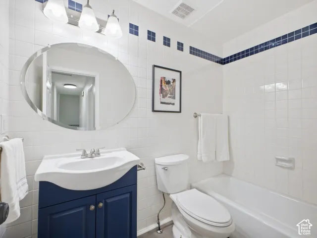White tiled bathroom featuring a navy blue vanity with an integrated sink, a white toilet, and a white bathtub