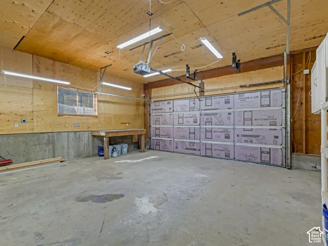Concrete flooring, wood-paneled walls, built-in workbench, overhead lighting, and an insulated garage door