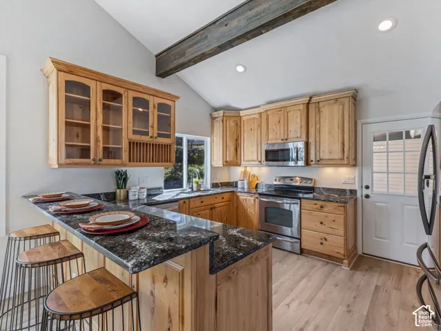 Vaulted ceiling with an exposed wood beam, recessed lighting, wood-finish flooring, and a kitchen island with a dark stone countertop