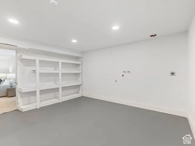 Recessed lighting, painted white walls, built-in shelving, concrete flooring, and an exposed pipe