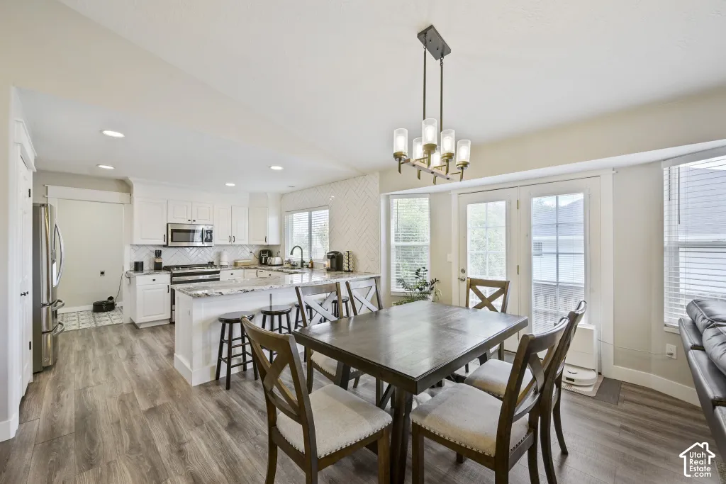 Wood-finish flooring, white cabinetry, stainless steel appliances, central kitchen island with seating, and double glass-paneled doors