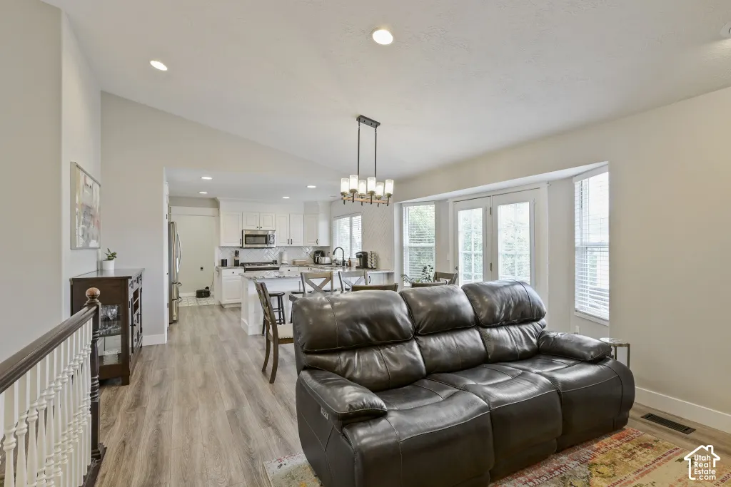Vaulted ceiling with recessed lighting, wood-finish flooring, white kitchen cabinetry, stainless steel appliances, and French doors