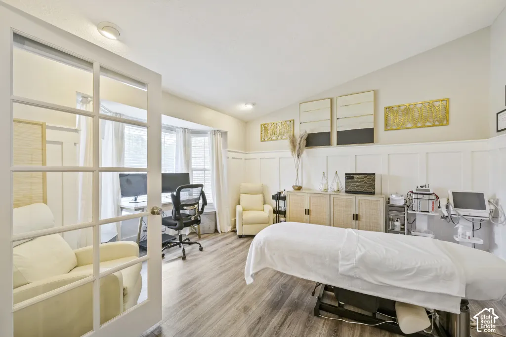 Spacious room featuring vaulted ceilings, wood-finish flooring, a bay window, and French doors