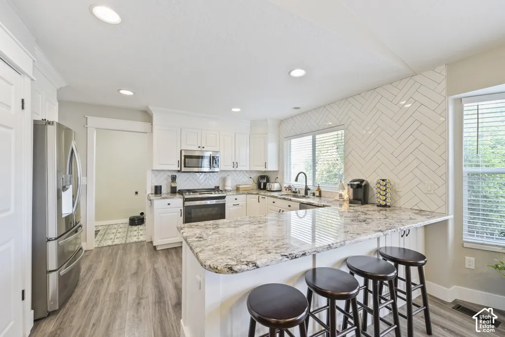 Well-appointed kitchen featuring white cabinetry, stainless steel appliances, a white herringbone tile backsplash, wood-finish flooring, and a large central island with seating