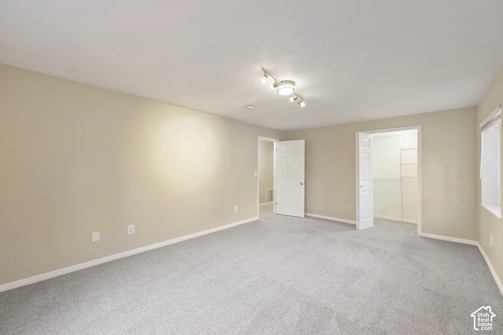 Neutral tone wall paint, track lighting, light grey carpeting, white trim, and a window with blinds
