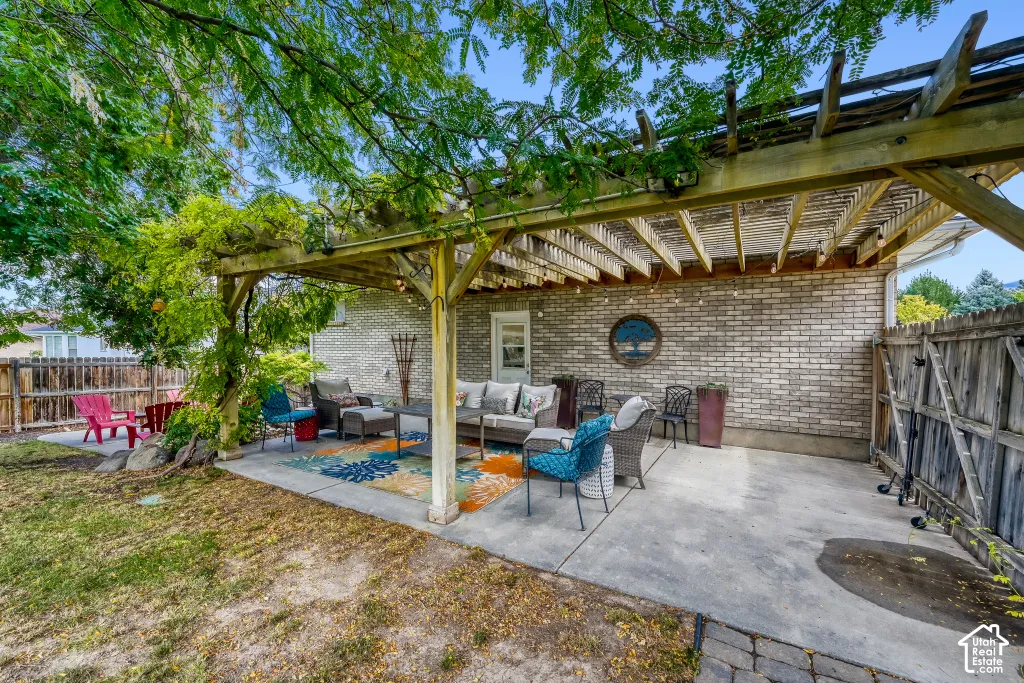 Expansive concrete patio with a wooden pergola, brick exterior, and wood fencing