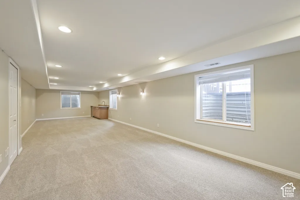 Expansive carpeted area with recessed lighting, multiple windows, a built-in wet bar with a sink, and wall sconces