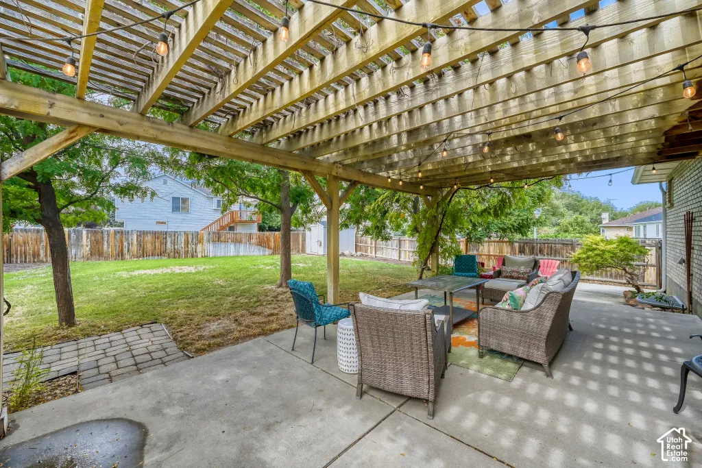 Expansive concrete patio with a wooden pergola, string lighting, and a fenced yard with mature trees