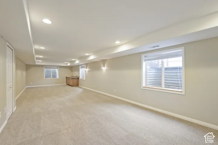 Expansive carpeted area with recessed lighting, multiple windows, a built-in wet bar with a sink, and wall sconces