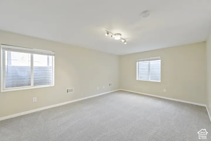 Expansive room featuring light-colored walls, recessed lighting, track lighting, and two windows with blinds